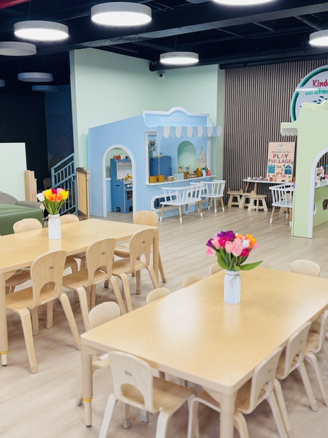 Main dining and activity area with wooden tables, green seating, and play village in background