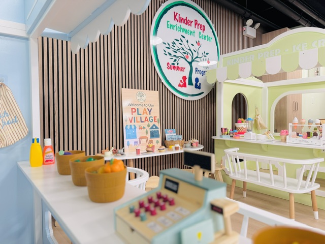 Interactive play village area with Kinder Prep signage, pretend kitchen, and cash register